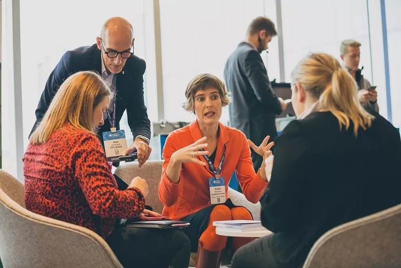 A group of people are sitting in a room discussing something and one of them is speaking.