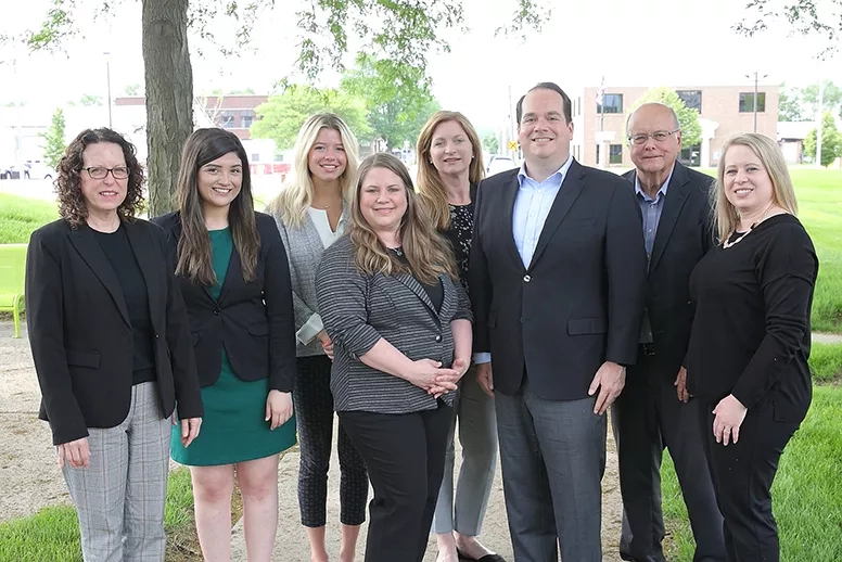 Group of eight employees smiling while posing for a picture in front of the building.