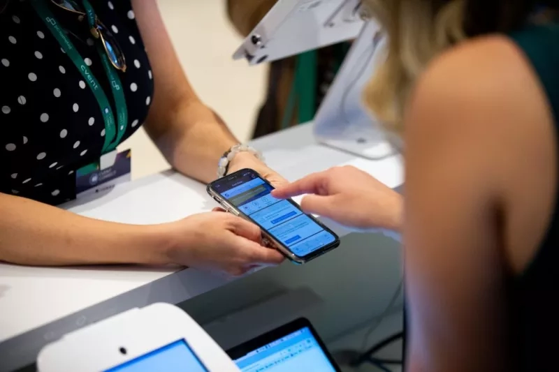 Two people with their phones, one wearing a black polka-dot shirt and a green lanyard.