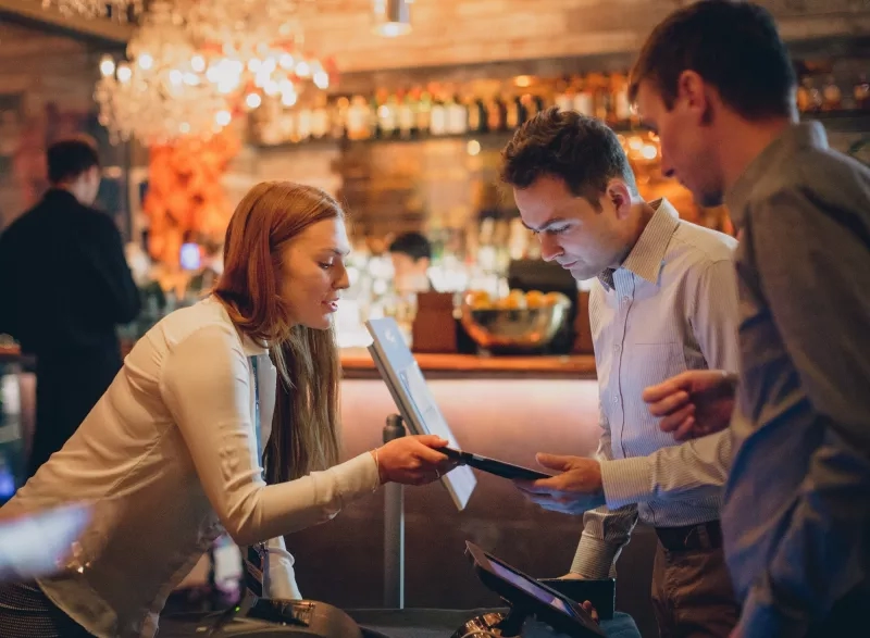 A woman and two men standing in front of a monitor in a restaurant.