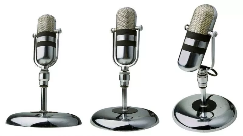 Three vintage silver and black microphones on a stand on a white background.
