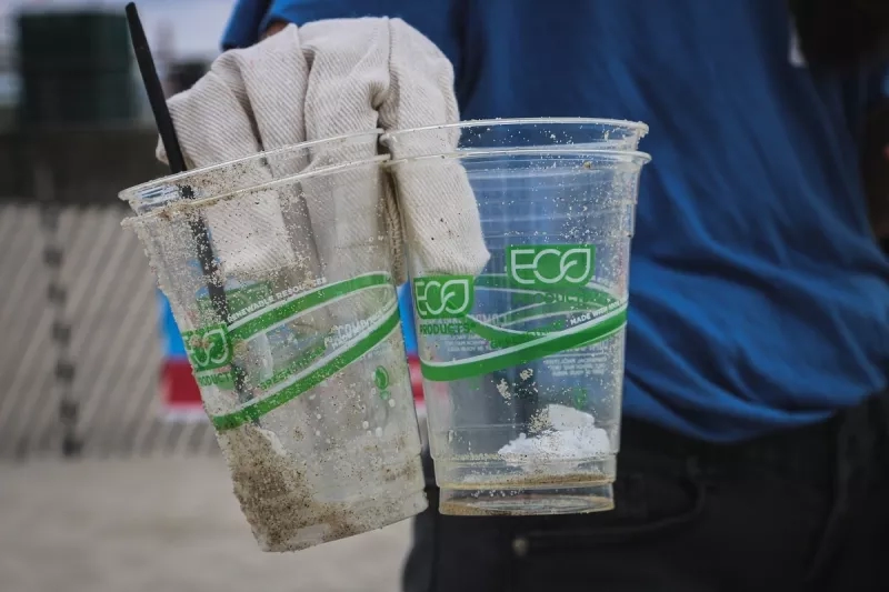 A man wearing gloves holds two cups made of single-use plastic, showing the text eco on them.