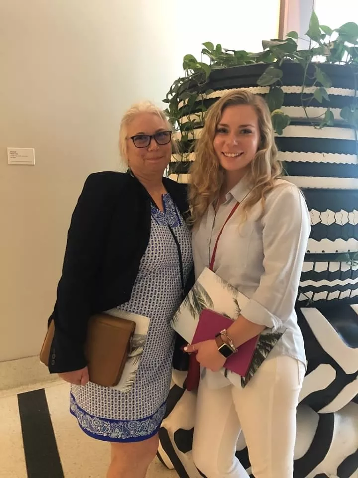 Two women standing next to each other smiling in front of a giant black and white pot.