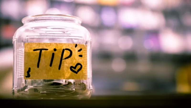 A jar with a "tip" label on it contains coins and bills inside.