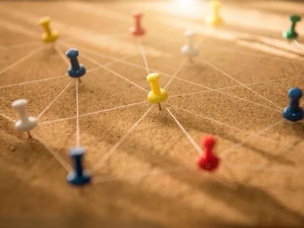 A close-up of a pin board with multi-colored pins and a web of white thread connecting them.