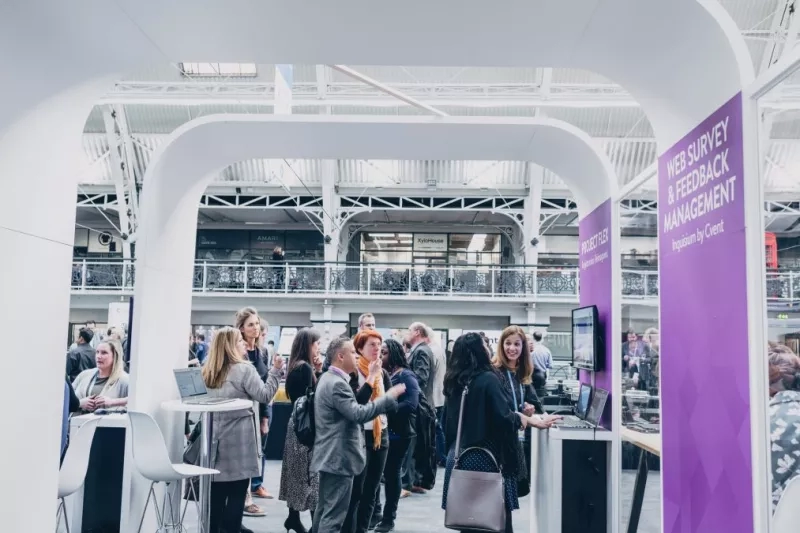 Group of people standing in front of a booth in an event in a large modern building.