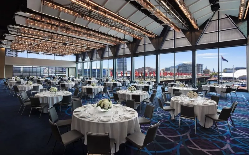 A large banquet hall at Hyatt Regency Sydney, featuring round tables, chairs, and a scenic view of the harbor.