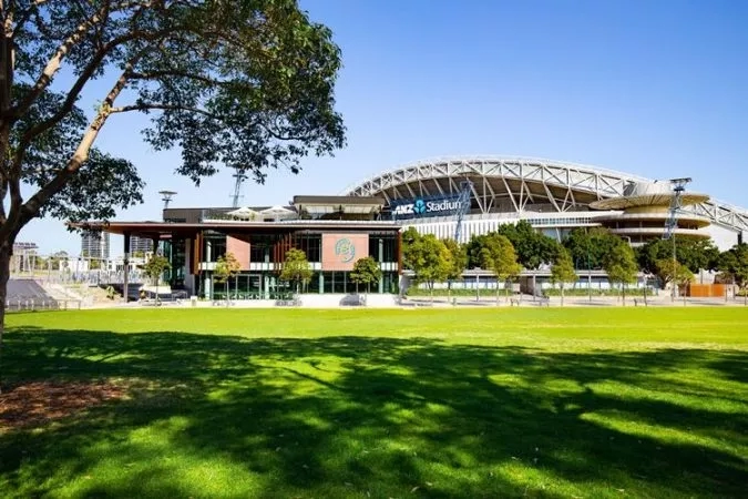 Green field with trees and a stadium in the background with ANZ Stadium written on the front.