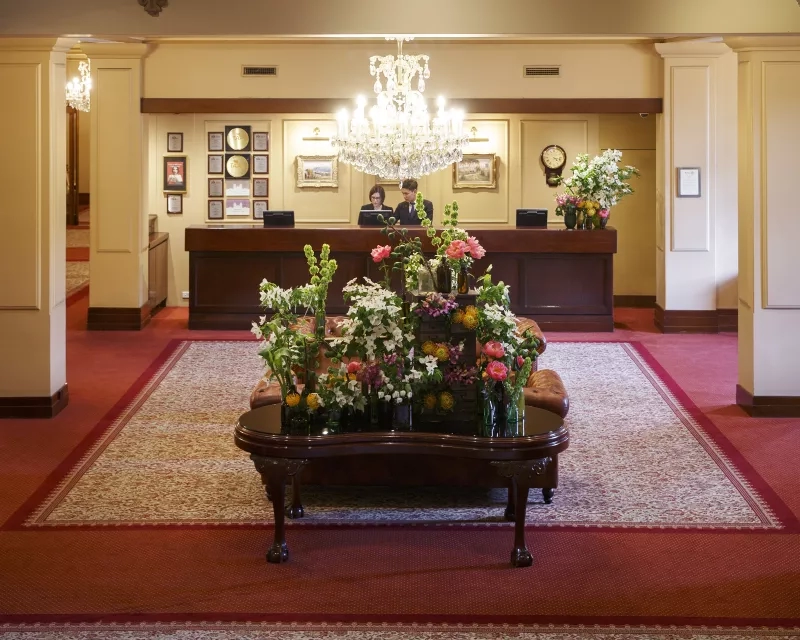 The Windsor Hotel lobby with a wooden reception desk and a floral centerpiece under a crystal chandelier.