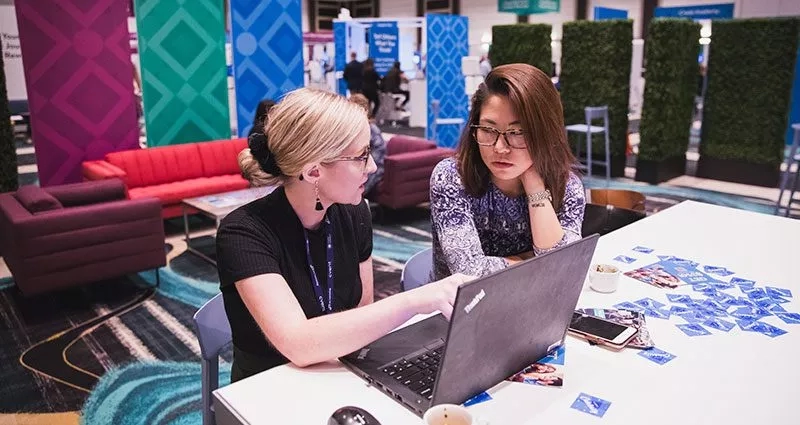 Two women sit at a laptop in an open, colorfully decorated space at CONNECT 2019.
