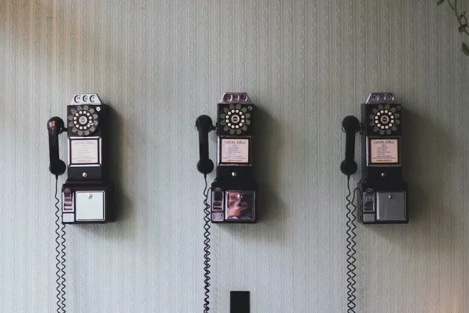 Three black telephones are mounted on a wall with a gray, textured pattern and a green plant.