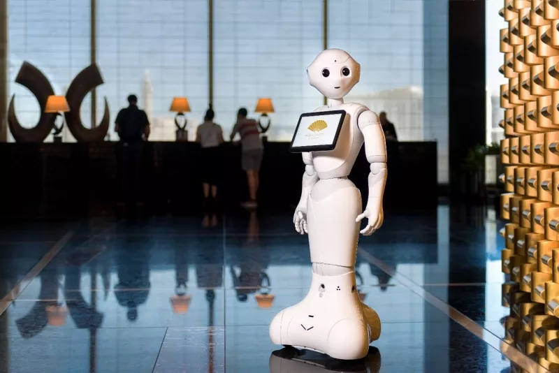 White Pepper robot with a tablet in its hands stands in front of a reception desk.