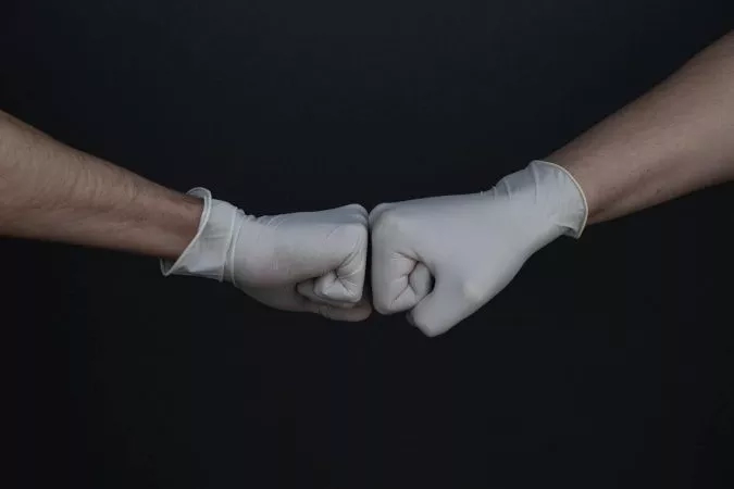 Two hands in white gloves clenched together in front of a black background.