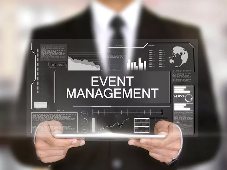 Businessman holding tablet with the words "Event Management" on it in front of blurred background.