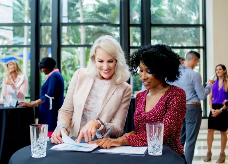 Two women are working on documents at a table at a convention at the Gaylord Palms Resort.
