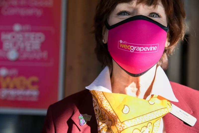 Woman wearing a face mask with the WeGrapevine logo on it in front of a sign.