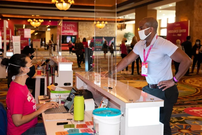 A woman is working behind a desk and a man is standing in front of her.
