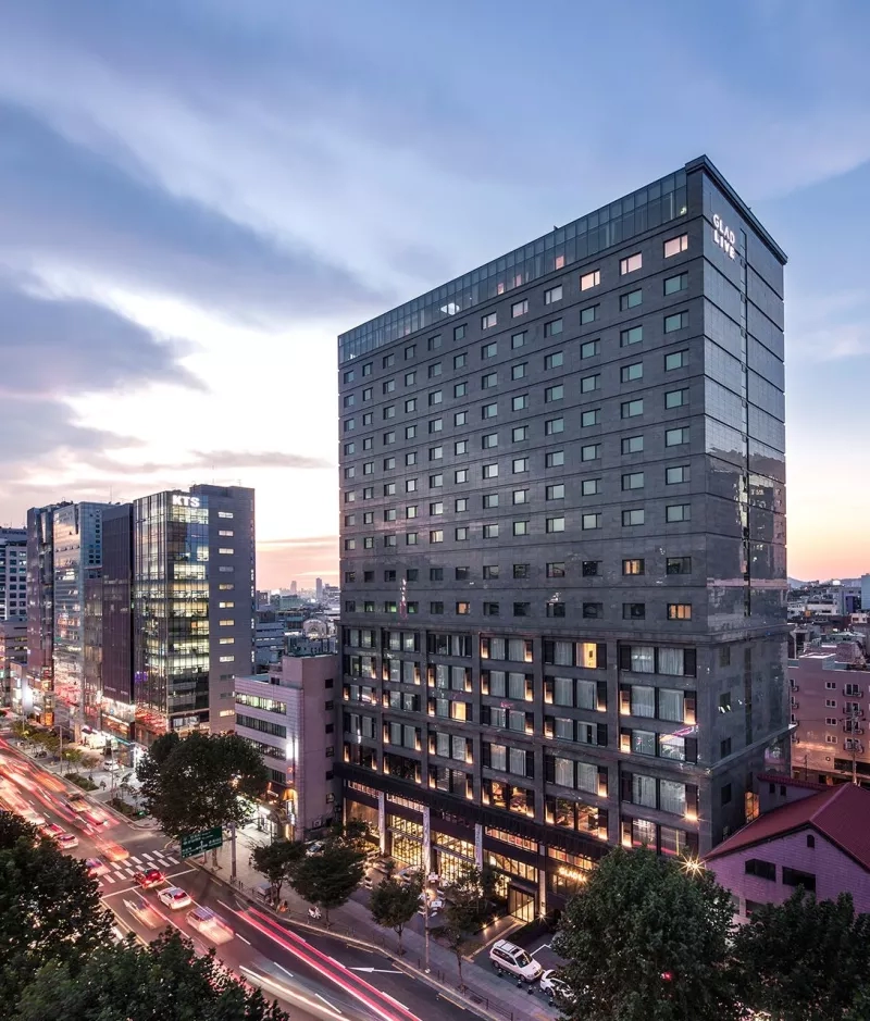Exterior view of Glad Live Hotel building with cars and trees in the foreground.