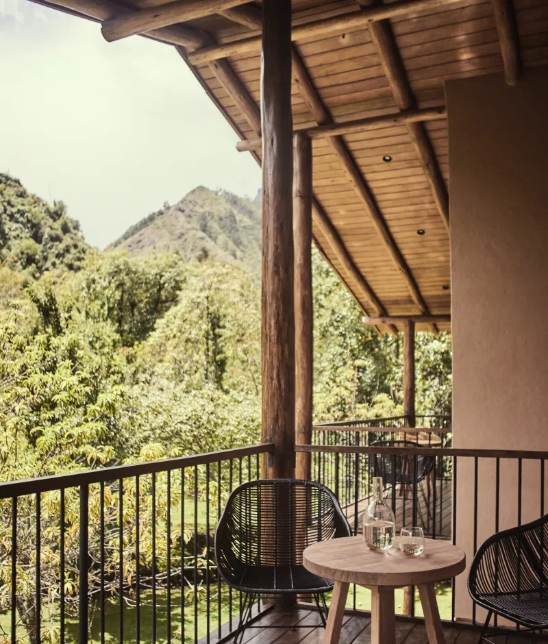 A wooden patio area with black chairs and a round table overlooking lush greenery and mountains.