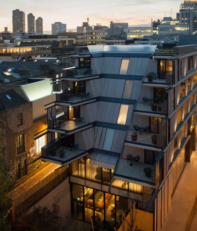 View of a modern building with many windows, balconies, and a terrace with potted plants.
