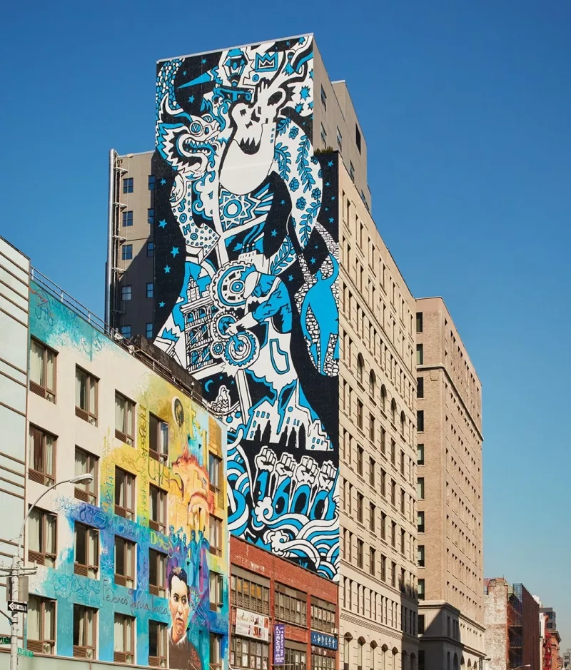 Tall buildings with large murals on the walls and a blue sky above them in NYC.