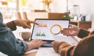 Two people pointing at a graph on a laptop screen in a coffee shop.
