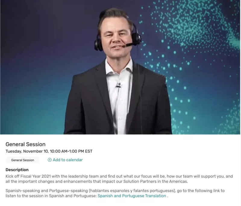 A man wearing a suit and headphones is standing in front of a blue background.