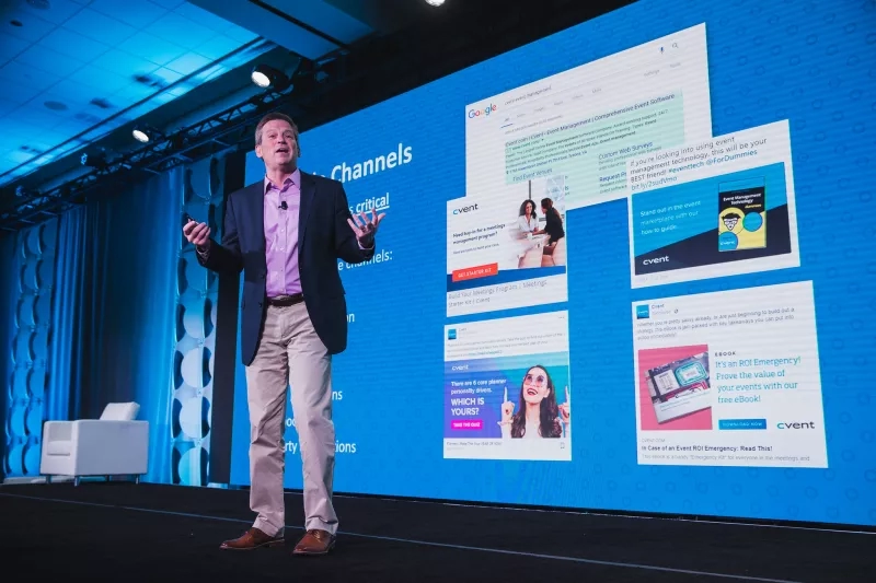 Presenter standing in front of a large screen with text and images, conference ambiance.