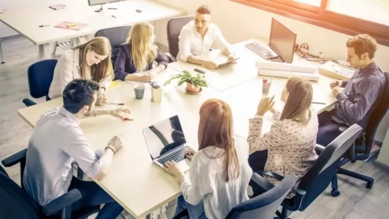 Group of people sitting at a table with laptops and papers, discussing event management best practices.