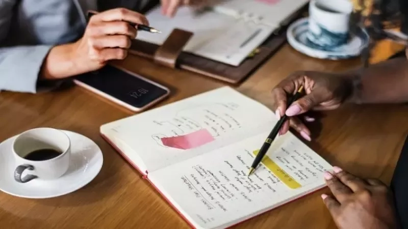 Two people sit at a table, discussing with notebooks and coffee, illustrating qualitative research methods in action.