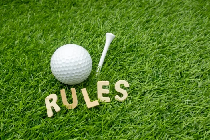 A golf ball and tee stick on a lawn with wooden letters spelling out "RULES".