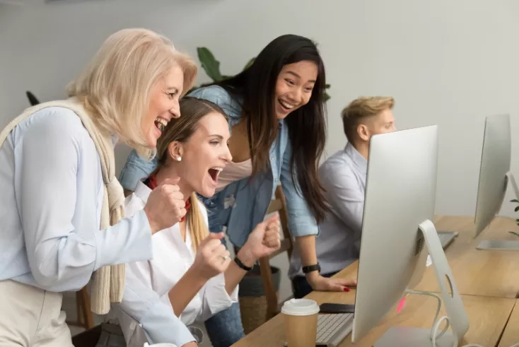 Group of people gathered around a computer laughing and cheering in an office.