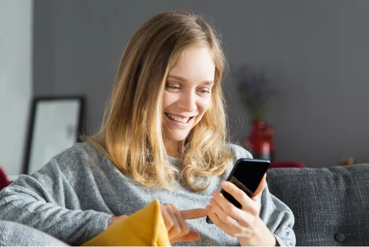A woman using her mobile phone while sitting on a couch in her living room at home.