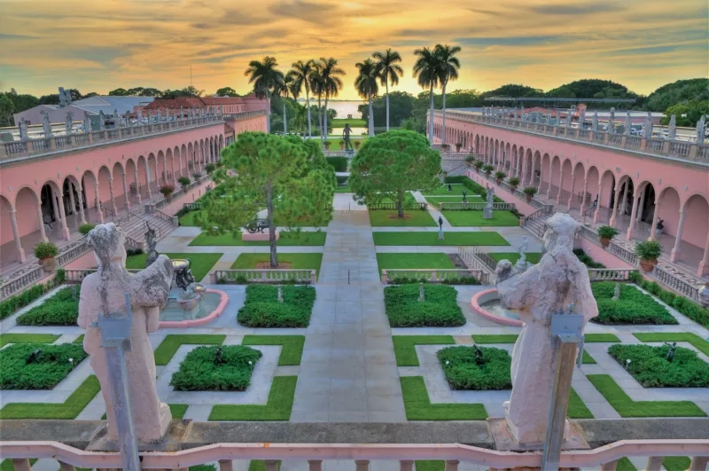 A view of the Ringling Museum courtyard with statues, architecture, landscaping, and a sunset sky.