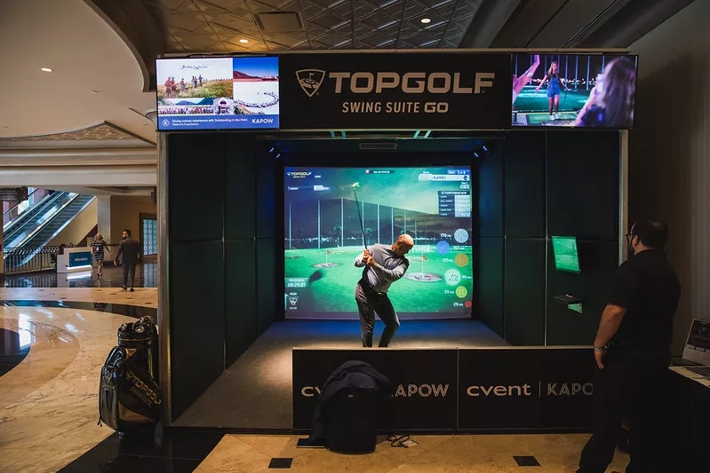 A man is playing golf on a screen inside the Topgolf Swing Suite Go inside a building.