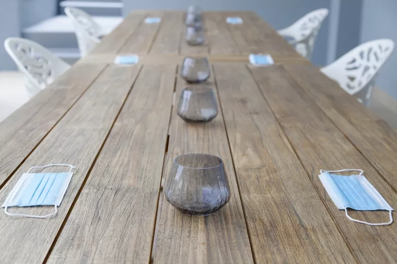 Glasses and masks on a wooden table outside with chairs in the background.