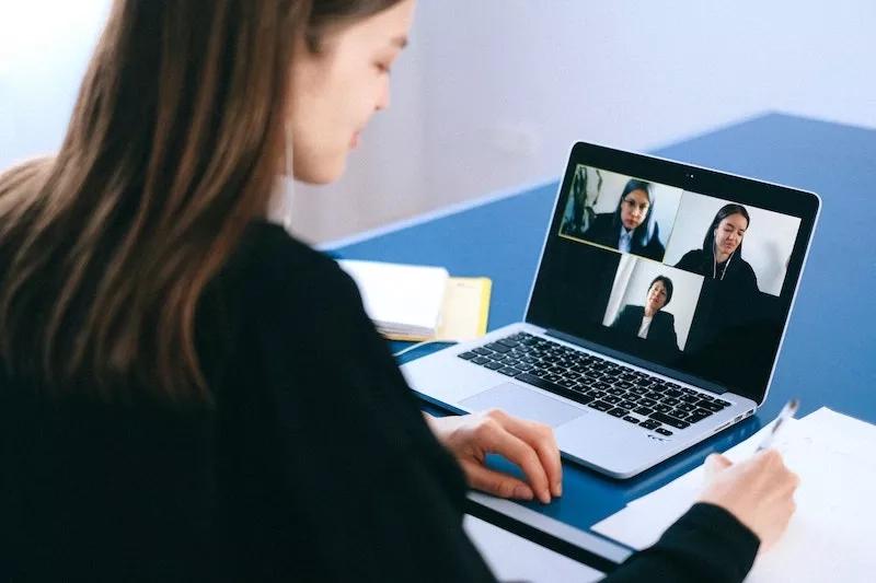 A woman is on a video call with other women on her laptop at a desk.