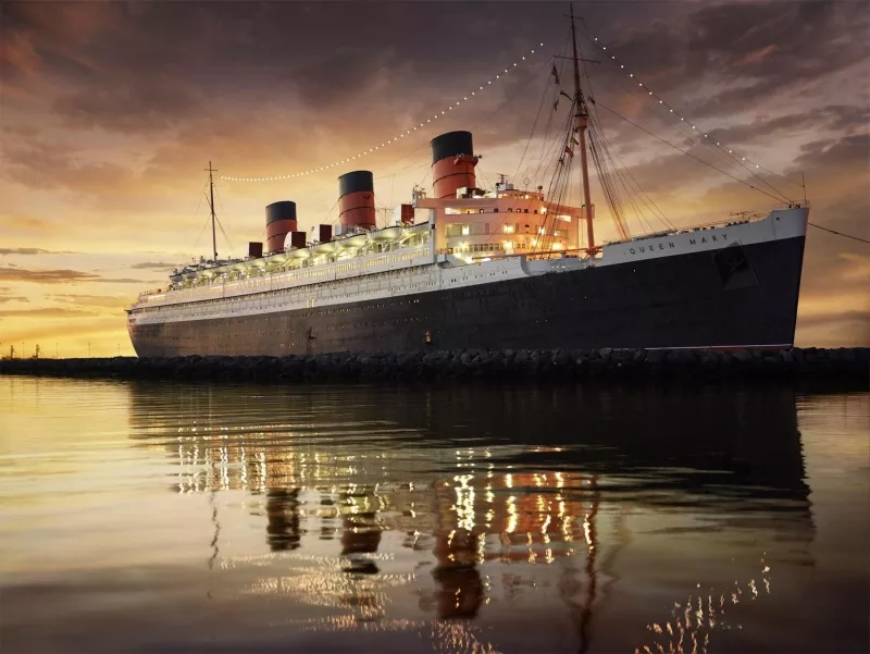 Queen Mary ship docked in a harbor at dusk with a calm sea and a cloudy sky.