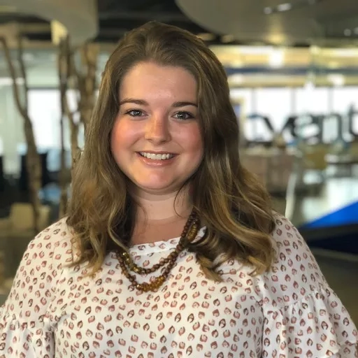 Amanda Guido, a smiling woman wearing a leopard print shirt and necklace, standing in a modern office.