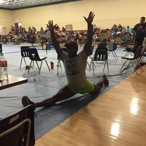 Gregory doing yoga pose with raised hands on blue mat in gym with people in background