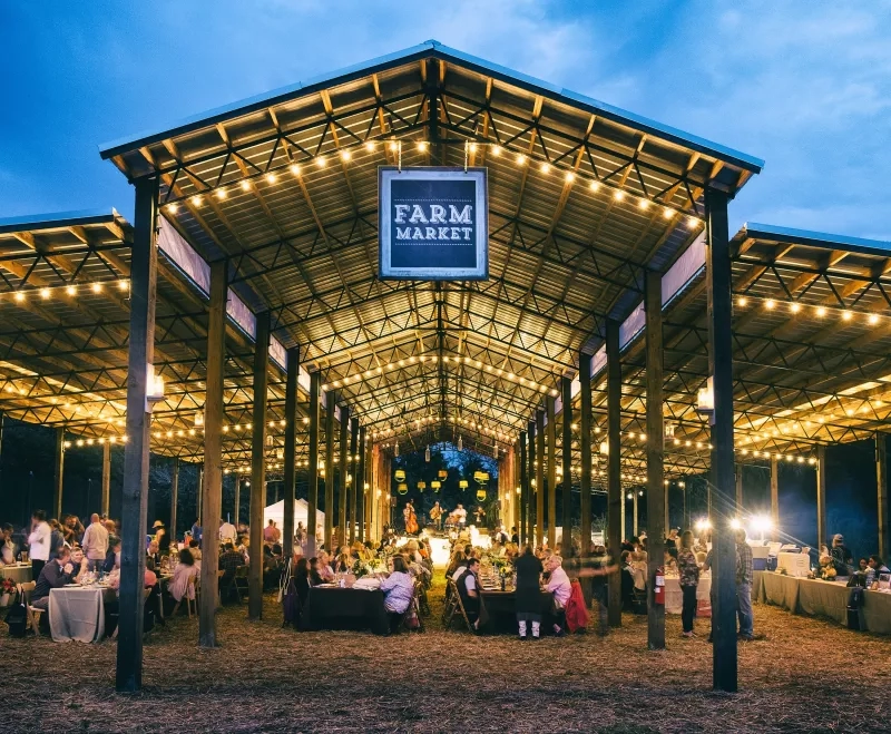 The Swank Farm Market, a large structure with an open-air dining area with tables, chairs, and many lights.