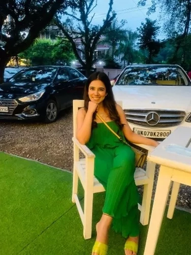 Riya, a model and influencer, sitting on a chair with Mercedes Benz cars in the background.