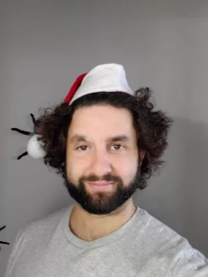 A man with curly hair wearing a Santa hat and a gray t-shirt.