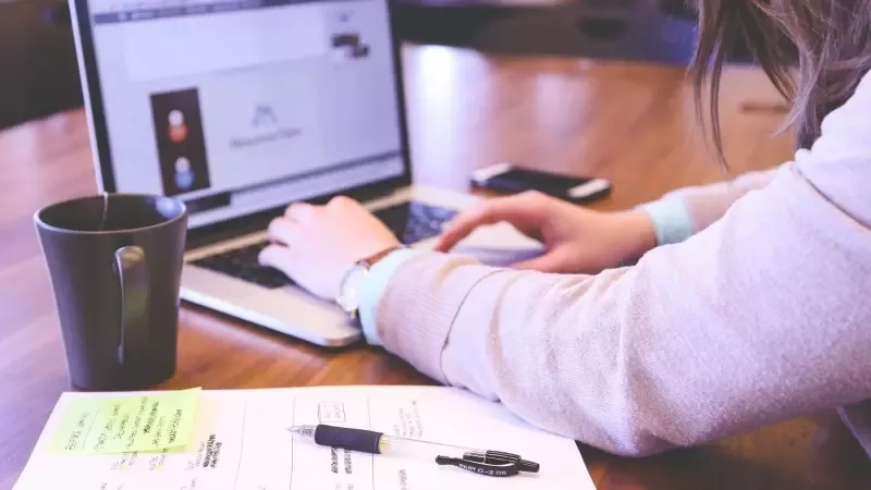 Woman typing on laptop with sticky notes and pen on desk, highlighting event planning efficiency.
