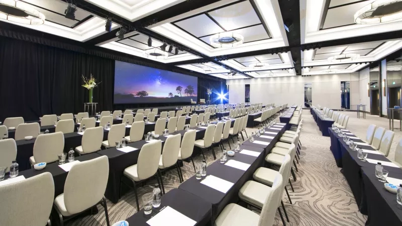 The function room in Shangri-La Sydney has a screen, chairs, and tables with bottles and cups on them.