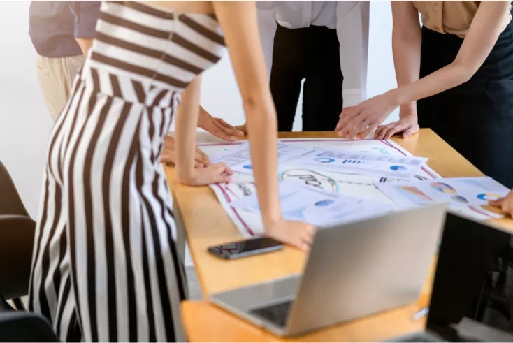 A group of people are planning with paper and a laptop on a table.