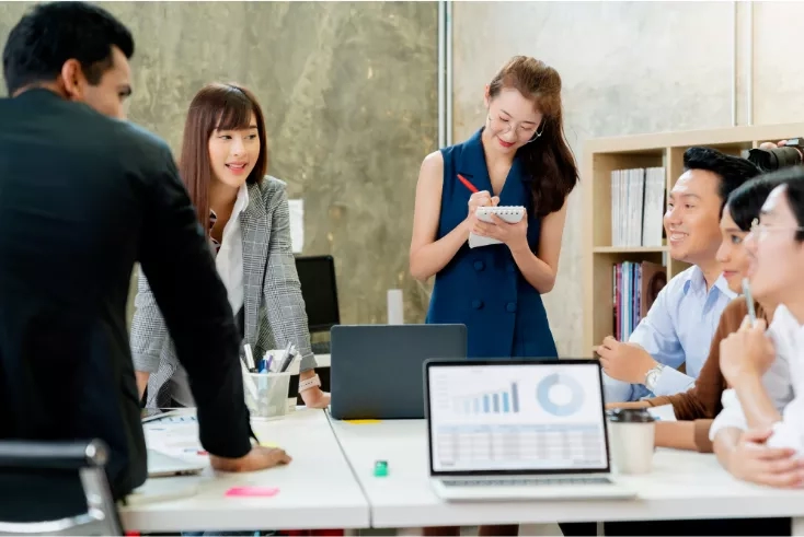 A group of people sitting around a table with laptops and a cup of coffee in the office.