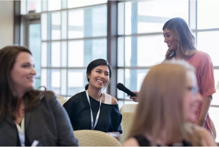 Three women are seated and one is interviewing another one at a conference.