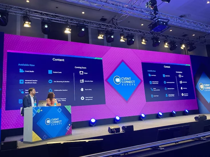 A man speaks on a stage with a woman and a screen with the words "Event Connect Europe".