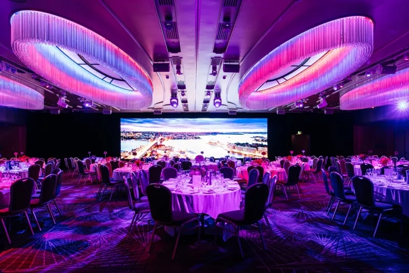 The Grand Ballroom I and II with round tables, purple lighting, and a large screen at the front.